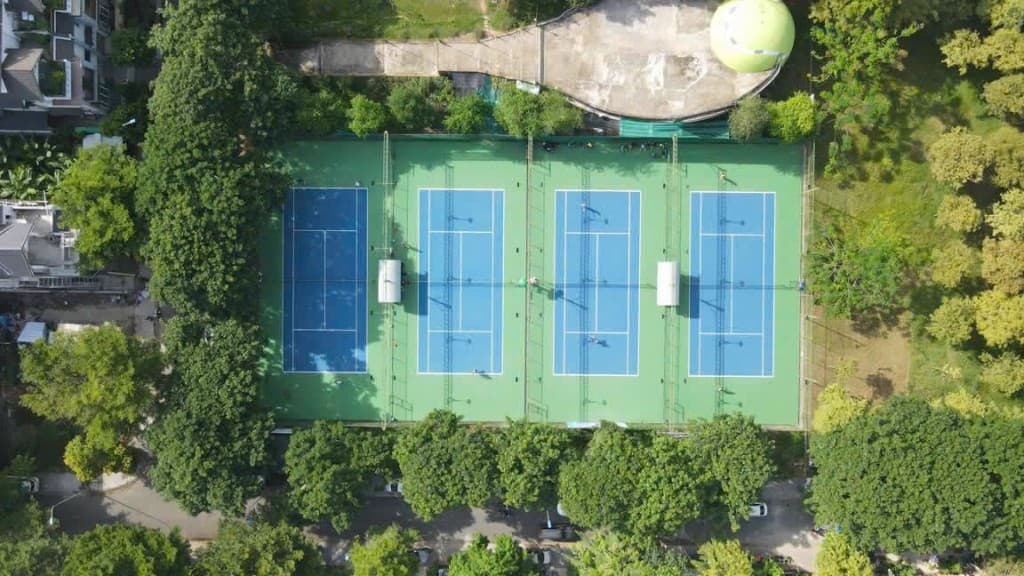 Toàn cảnh từ trên cao bốn sân tennis bao quanh bởi cây xanh